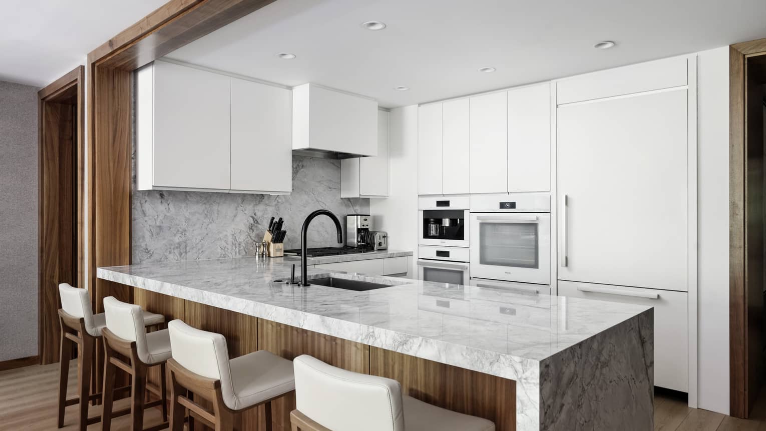 Modern kitchen with white cabinetry and a marble island and four bar seats