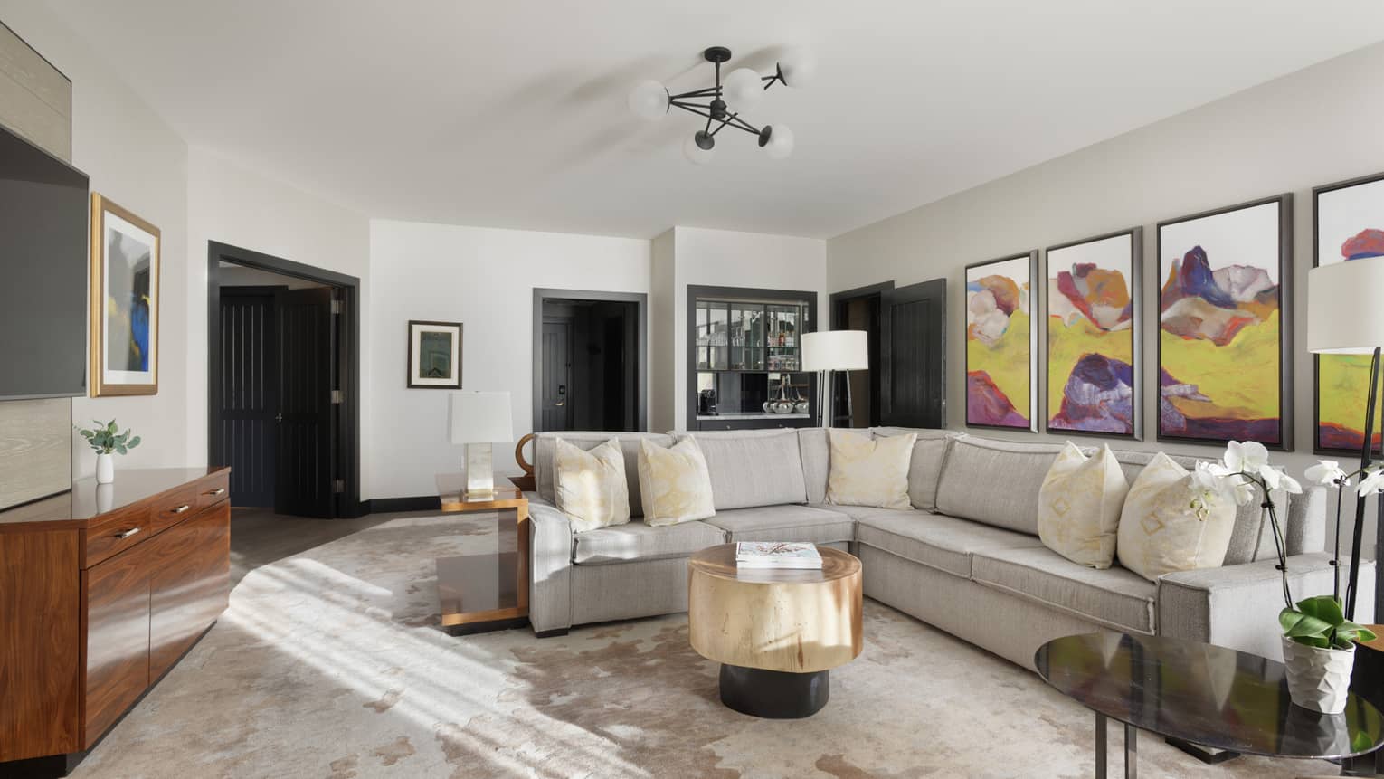 Living room with light grey sectional sofa and four pieces of purple and yellow artwork on the wall