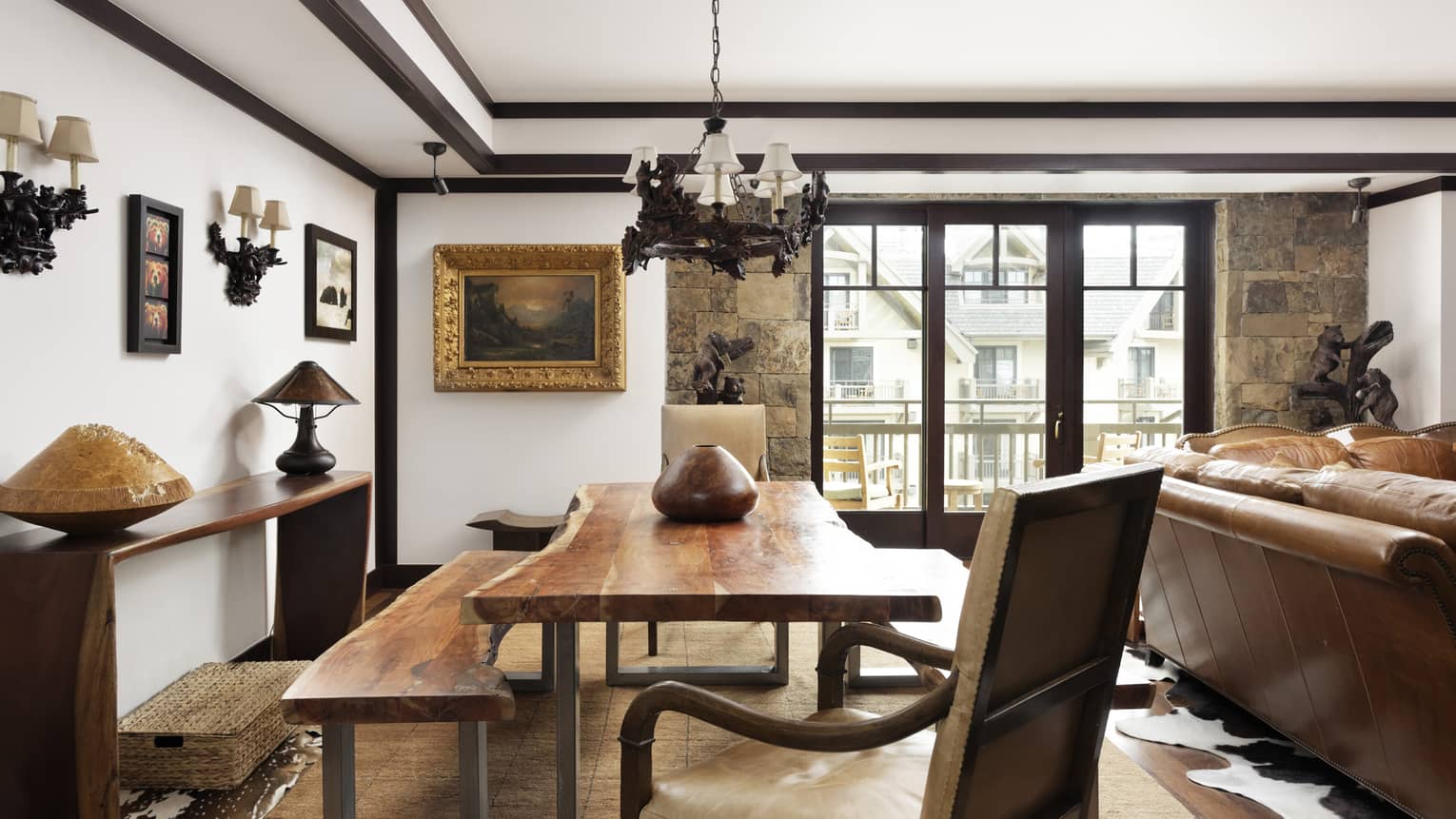 Large dining table made of rustic wood, matching bench, chandelier, windows