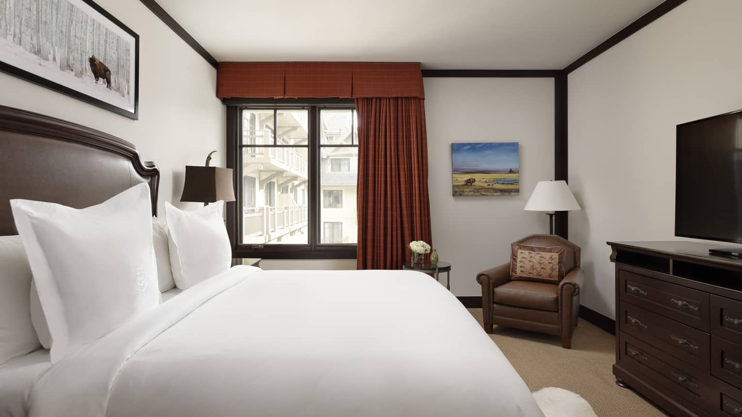 Bedroom with king bed, leather headboard, dark red curtains, tan carpet, leather armchair