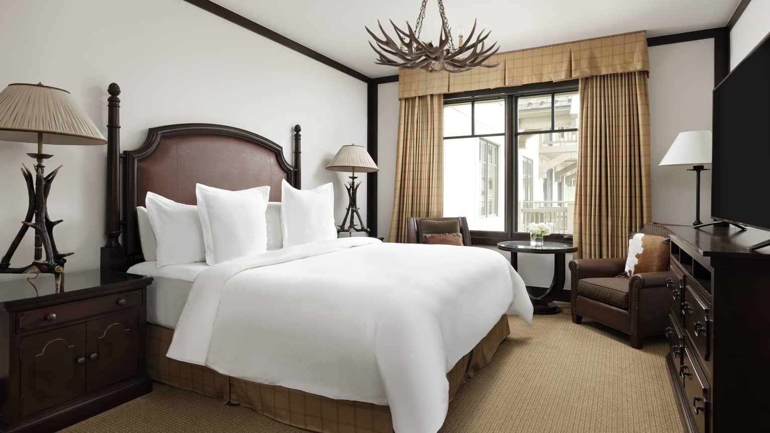 Bedroom with king bed, leather headboard, tan curtains and carpet, antler-like lighting