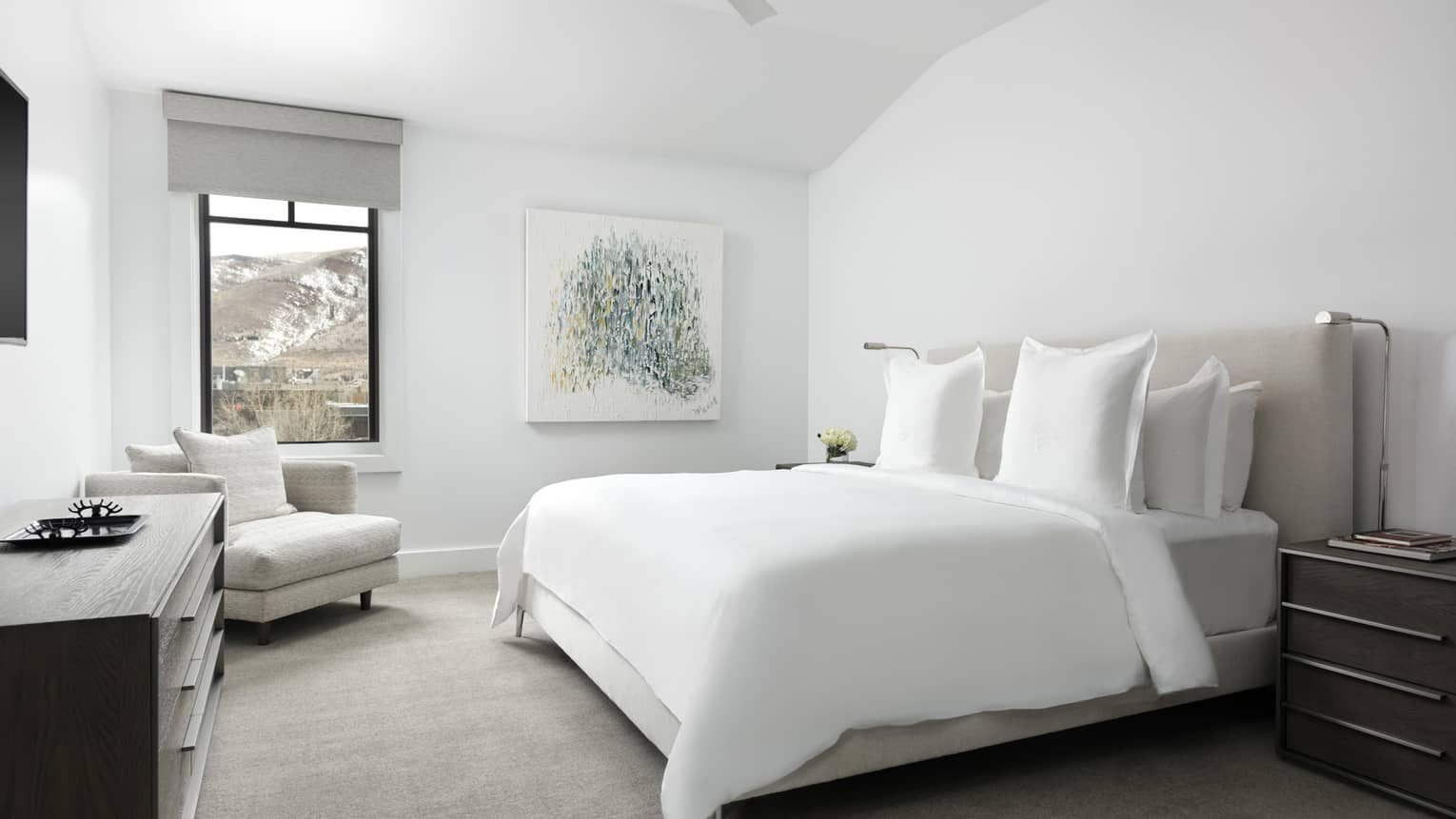 Bedroom with white walls, white king bed, light grey arm chair, dresser, window