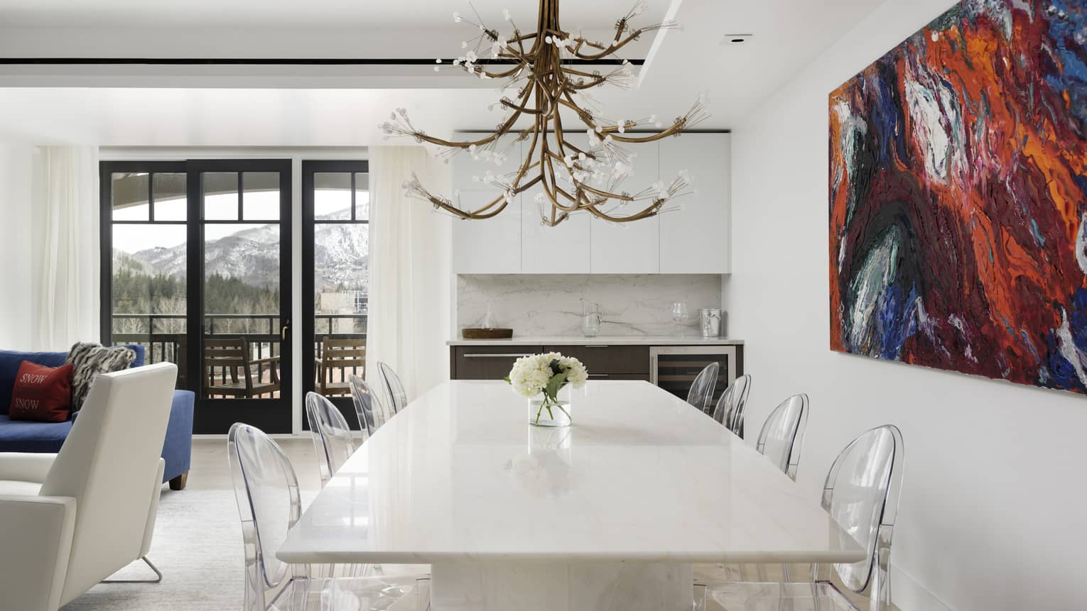 Dining room with white table, eight clear chairs, chandelier, blue and red artwork on wall
