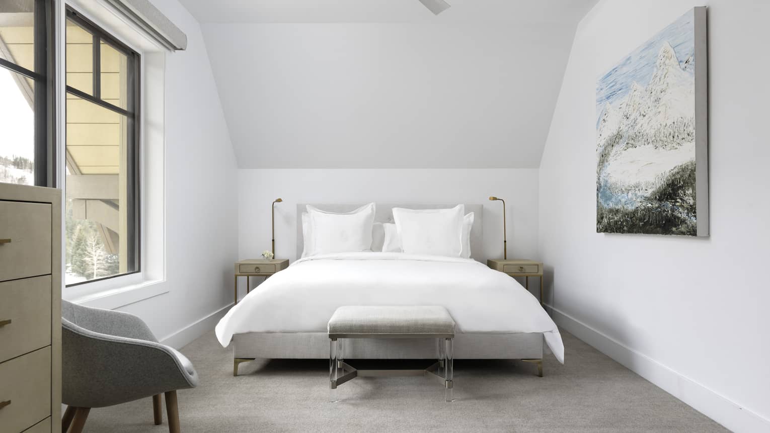 Bedroom with white walls, white king bed, light grey chair, artwork, window