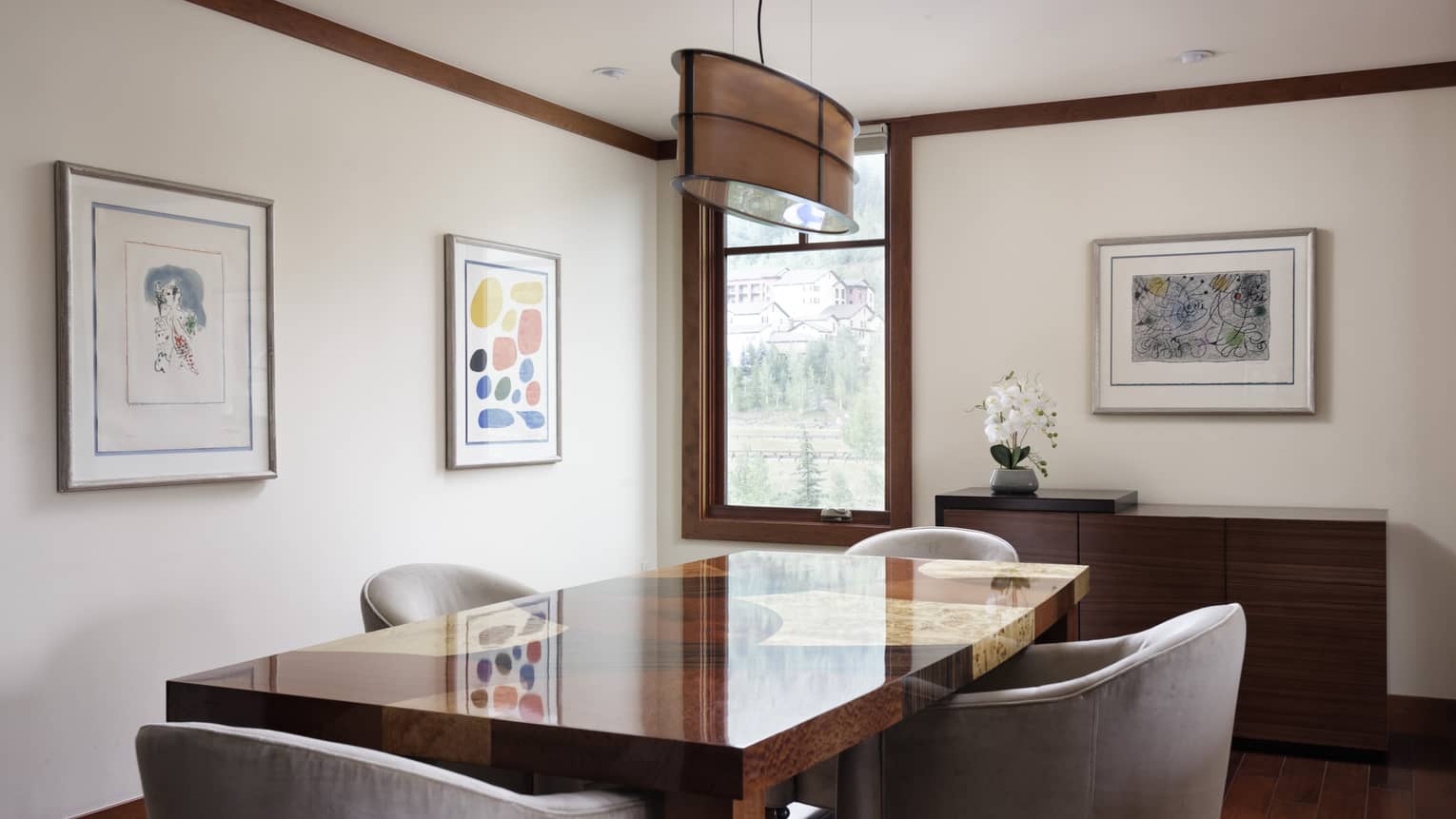 Dining room with wooden table, four grey chairs, cream walls, three framed artwork