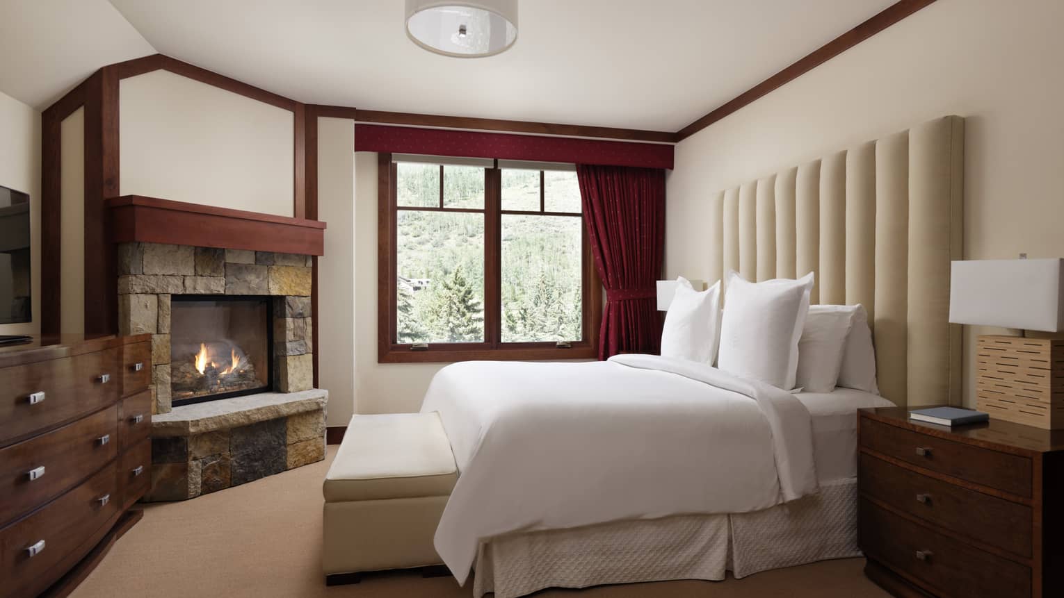 Bedroom with large upholstered, cream-coloured headboard, stone fireplace