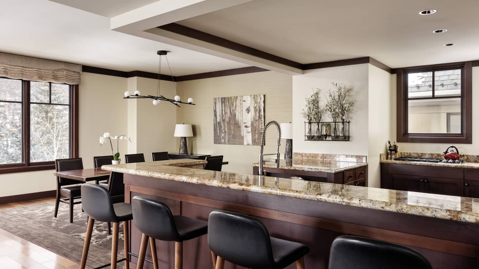Kitchen with granite countertops and dark wood cupboards, and a counter and four black leather bar seats