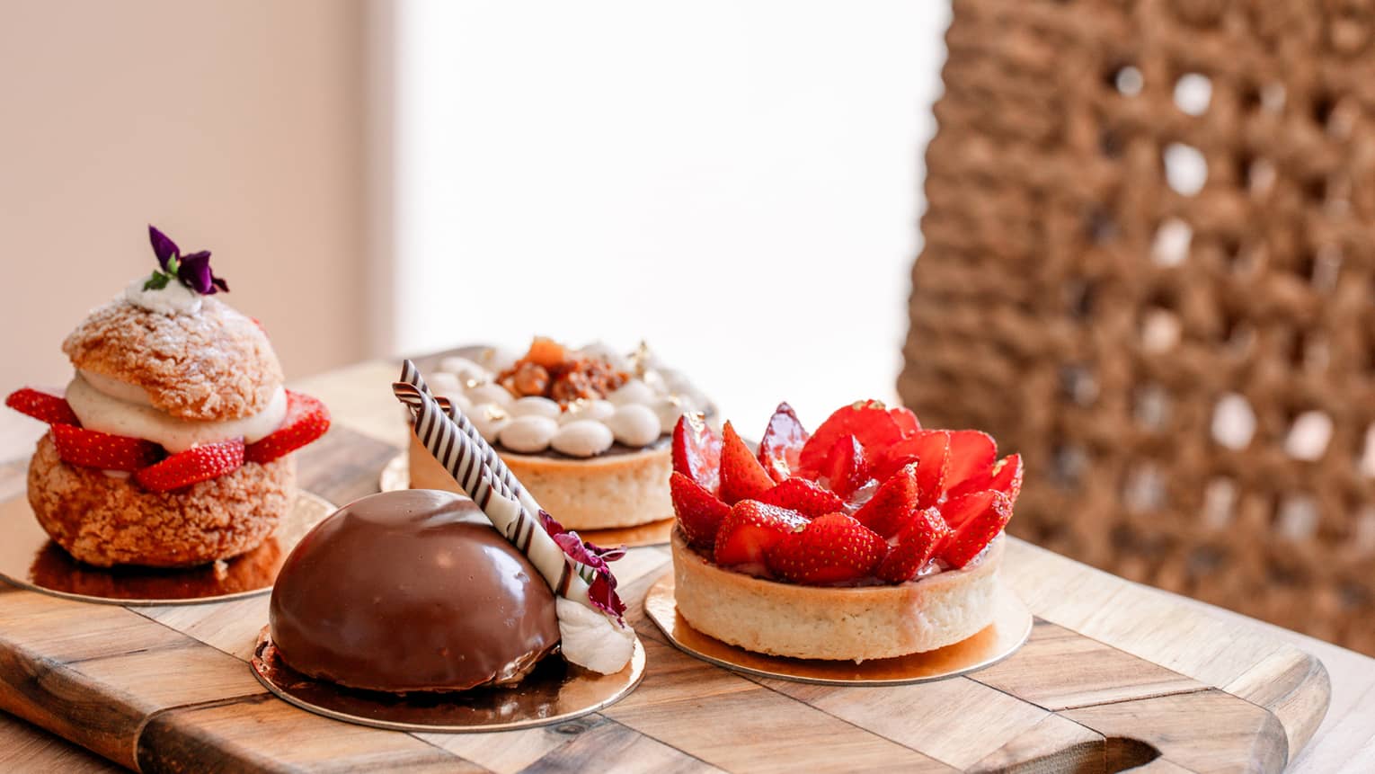 Four gourmet mini pastries, including a strawberry tart and a chocolate dome cake