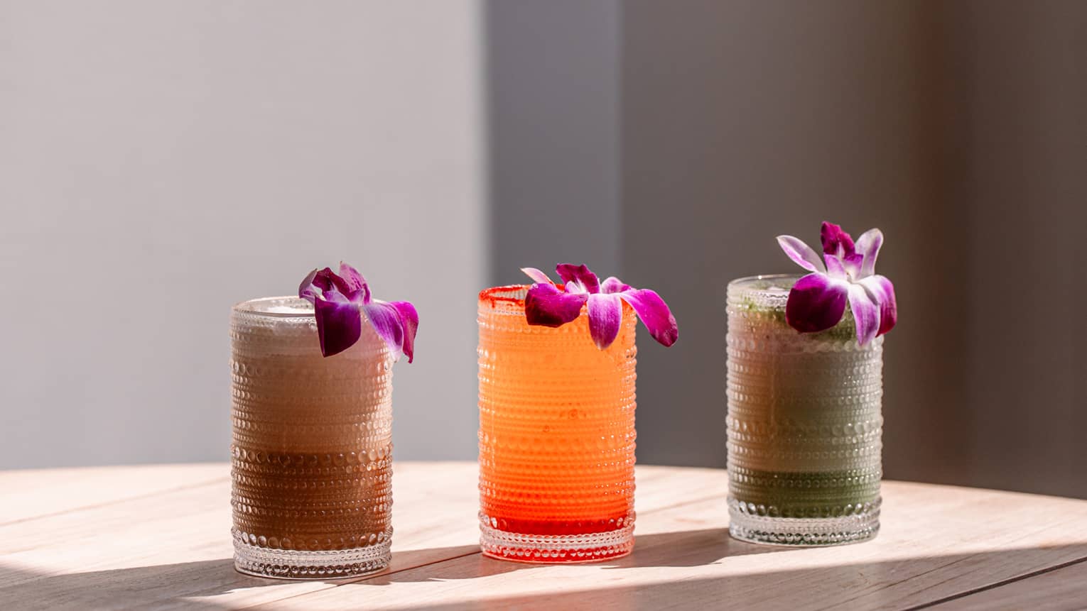 Three juice glasses, each with purple Hawaiian flower
