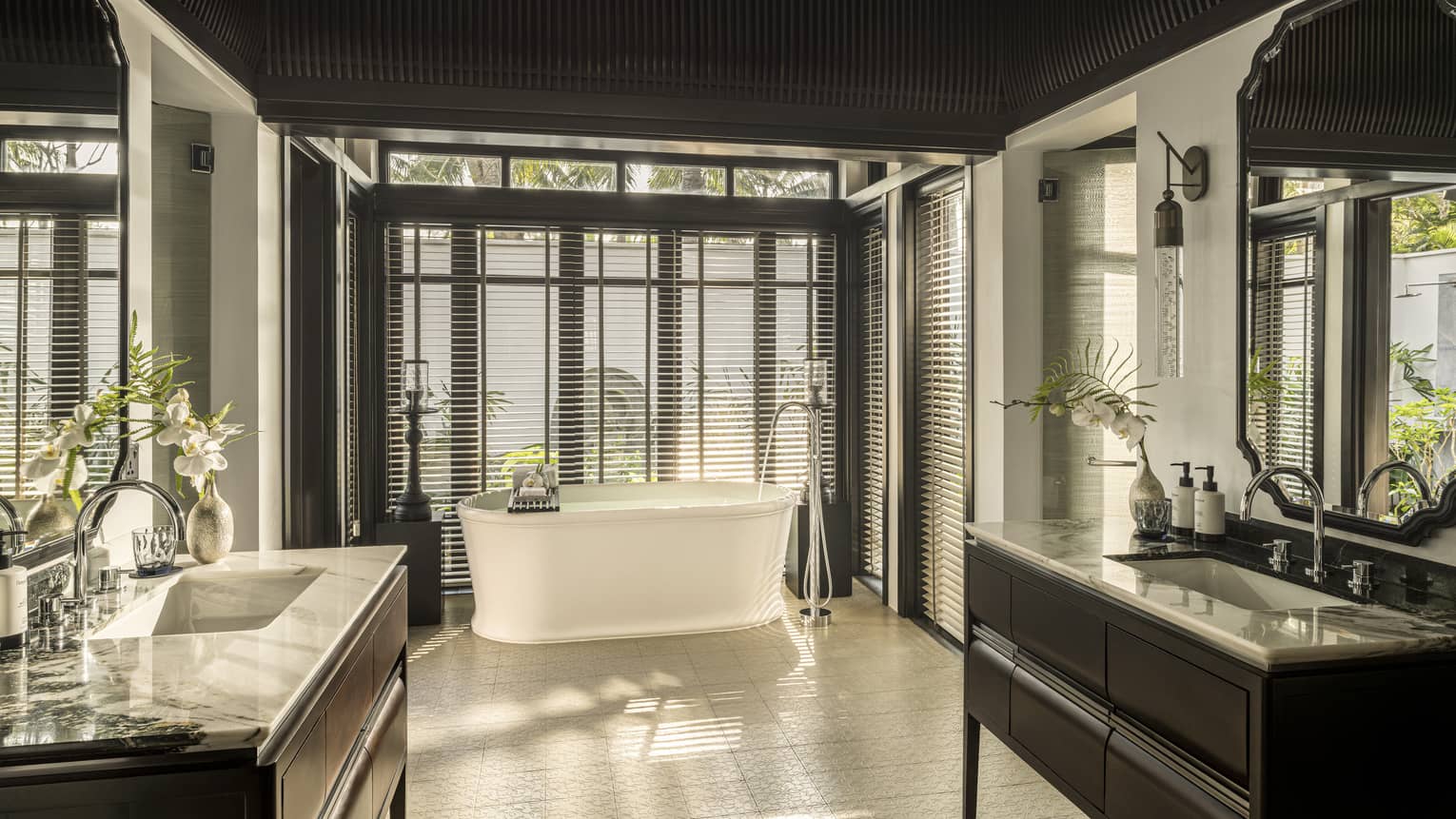Large luxury bathroom of resort villa, featuring a vanity on each side of the bathroom and a freestanding tub next to a wall of windows