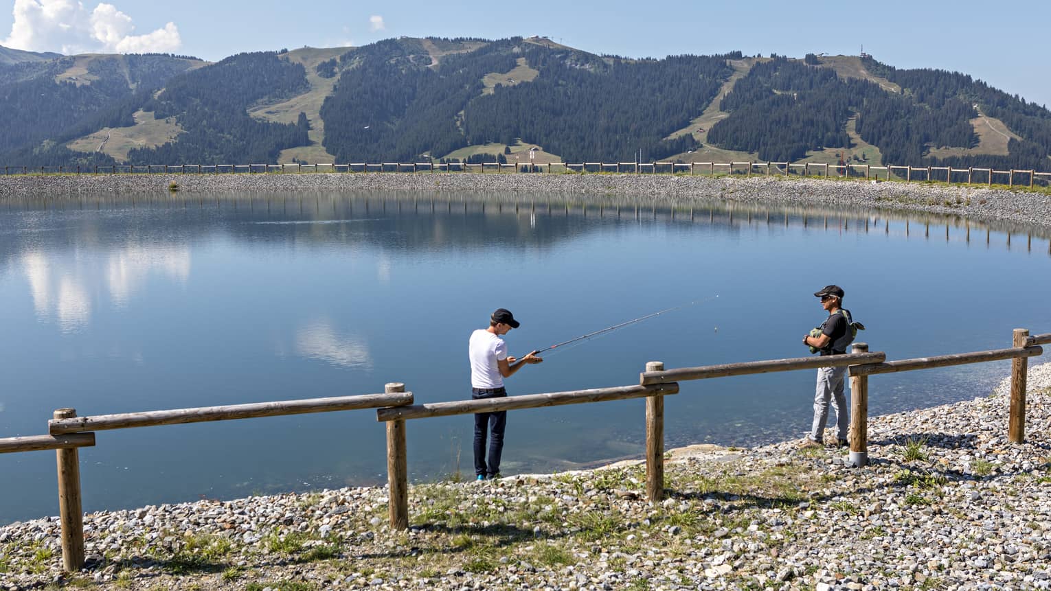 Mont d’Arbois, two men fishing in pond in front of wood fence, mountains in background