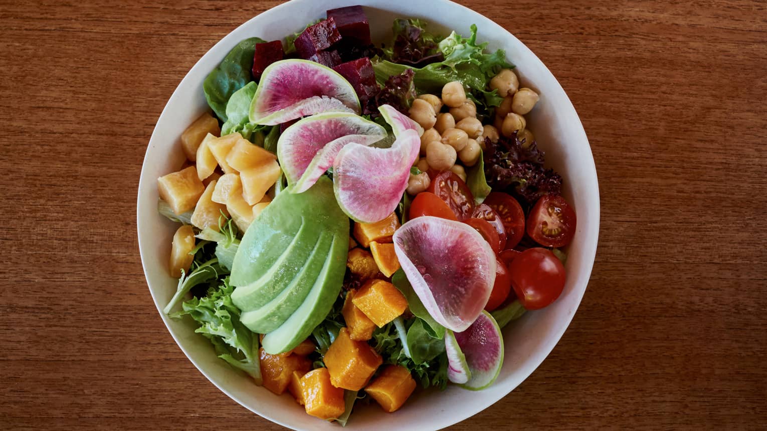 Aerial view of bowl with fresh chopped greens, vegetables, avocado slices, chickpeas