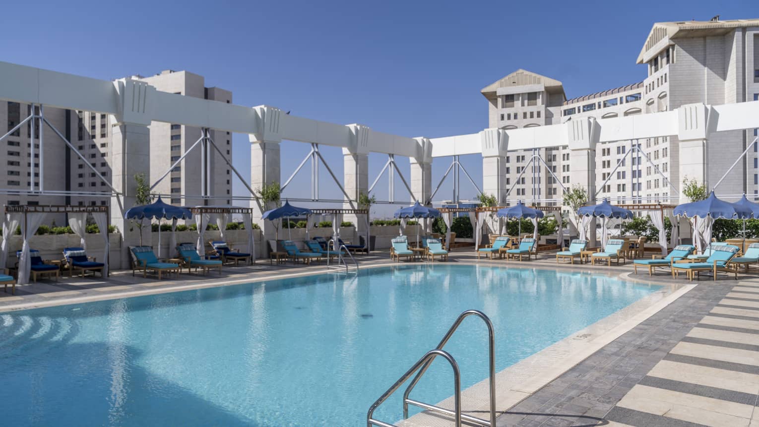 Outdoor pool surrounded by teal lounge chairs and white columns