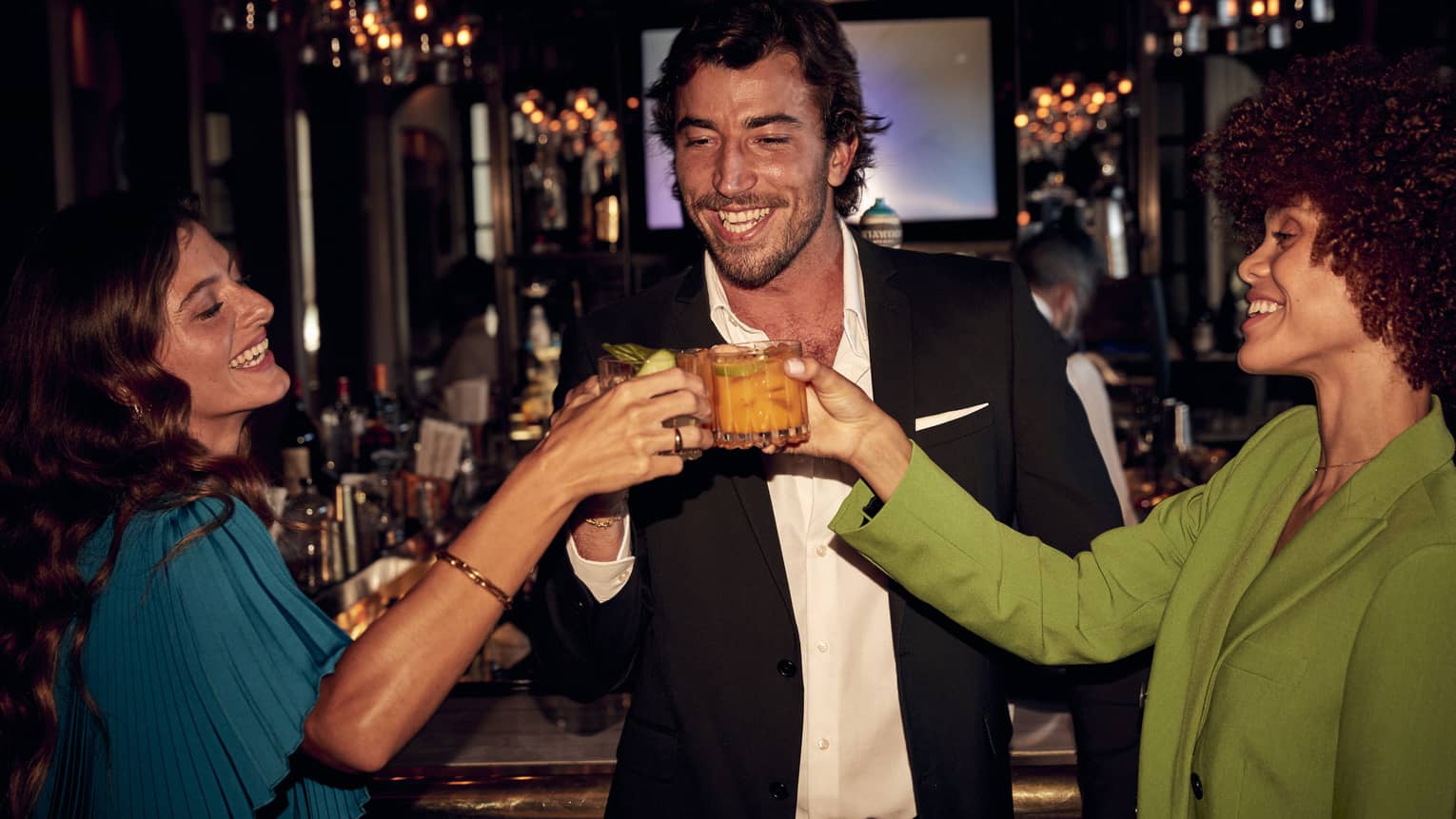 A man and two women toasting with drinks in hand at a bar.