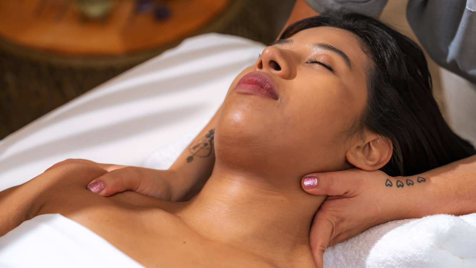 Woman relaxes with eyes closed as massage therapist massages her neck