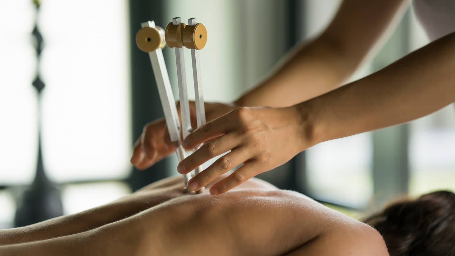 Masseuse uses wood tool on woman's spine, bare back in spa
