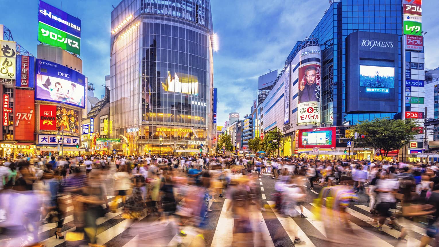 Image of blurry crowds along sidewalk under glass buildings, colourful billboards at night