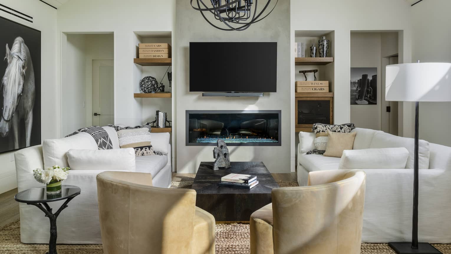 Luxury villa living room with white sofas, beige armchairs, wall-mounted TV, linear fireplace, built-in shelves with decor and black-and-white horse artwork