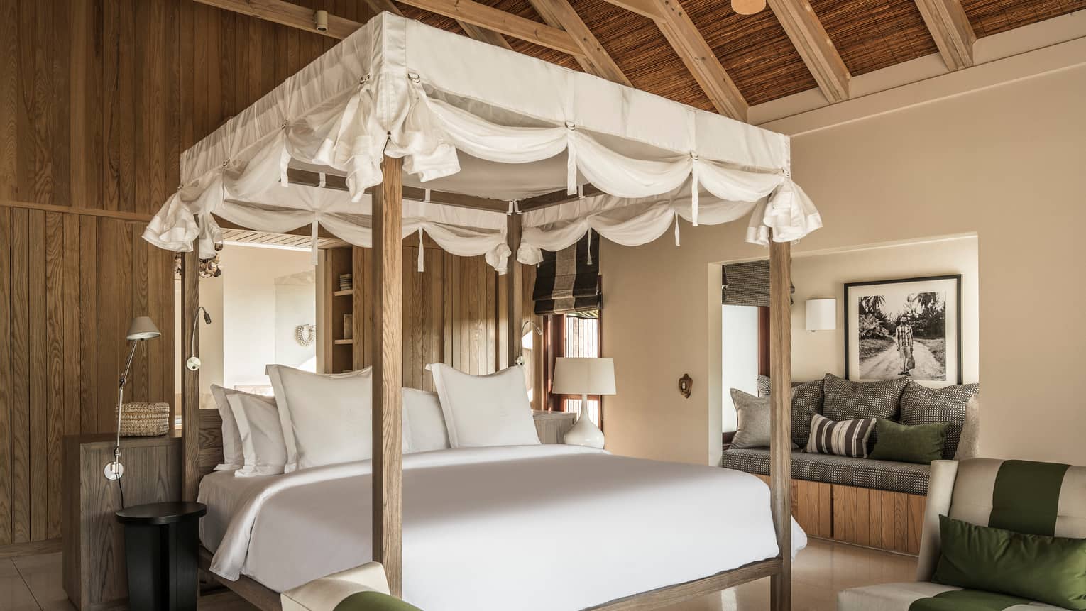 White canopy with ties at top of poster bed, behind sofas and cushioned bench