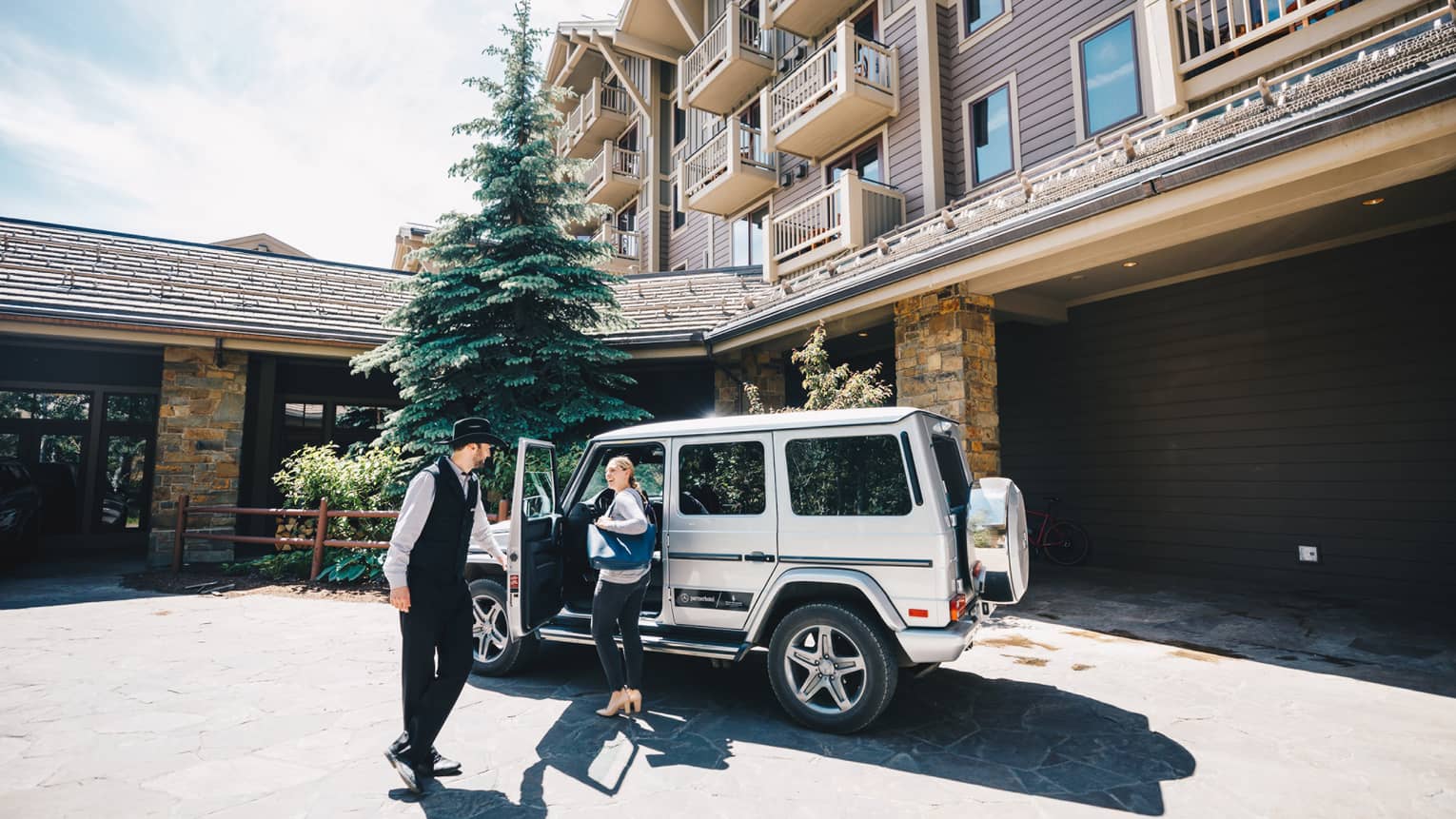 Resort staff opens the driver-side door of a luxury utility vehicle parked in the driveway for guest