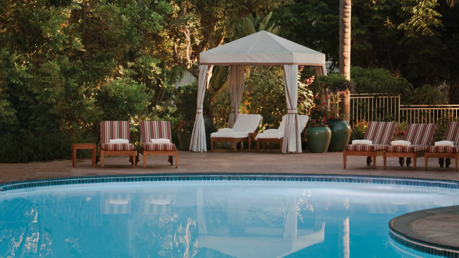 Striped pool chairs, white lounge chairs under white cabana curtains on swimming pool deck