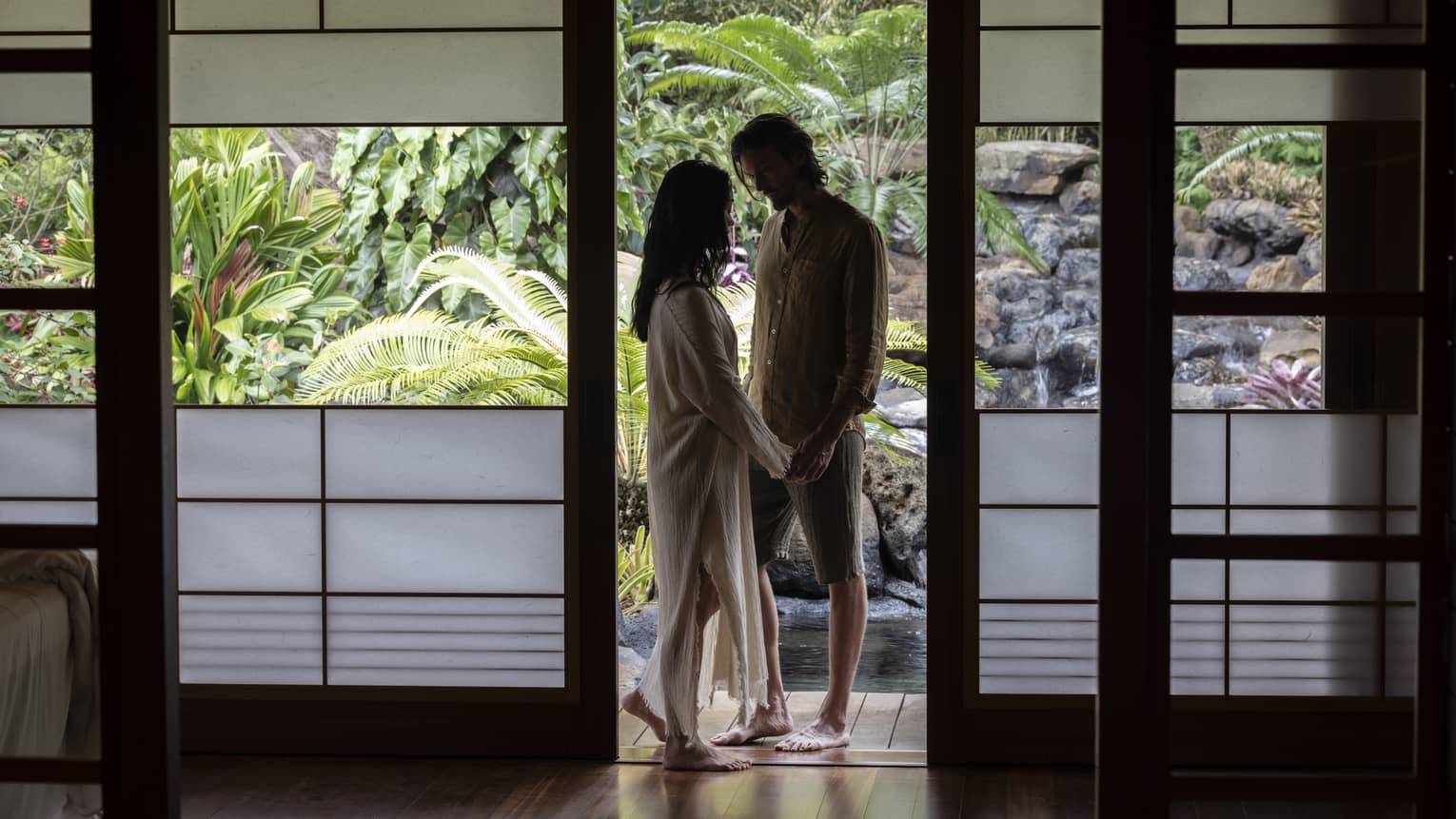 Man and woman stand visible in a garden setting, through frosted doors of a private spa hale