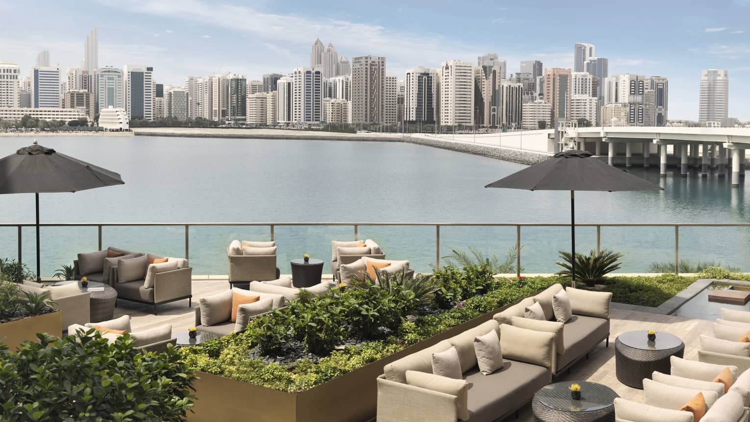 Outdoor sofas, umbrellas and planters on patio overlooking water, city