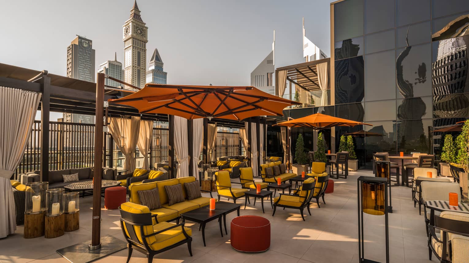 Rooftop patio with plush yellow patio furniture, large orange umbrellas, wood pergolas, city skyline in background