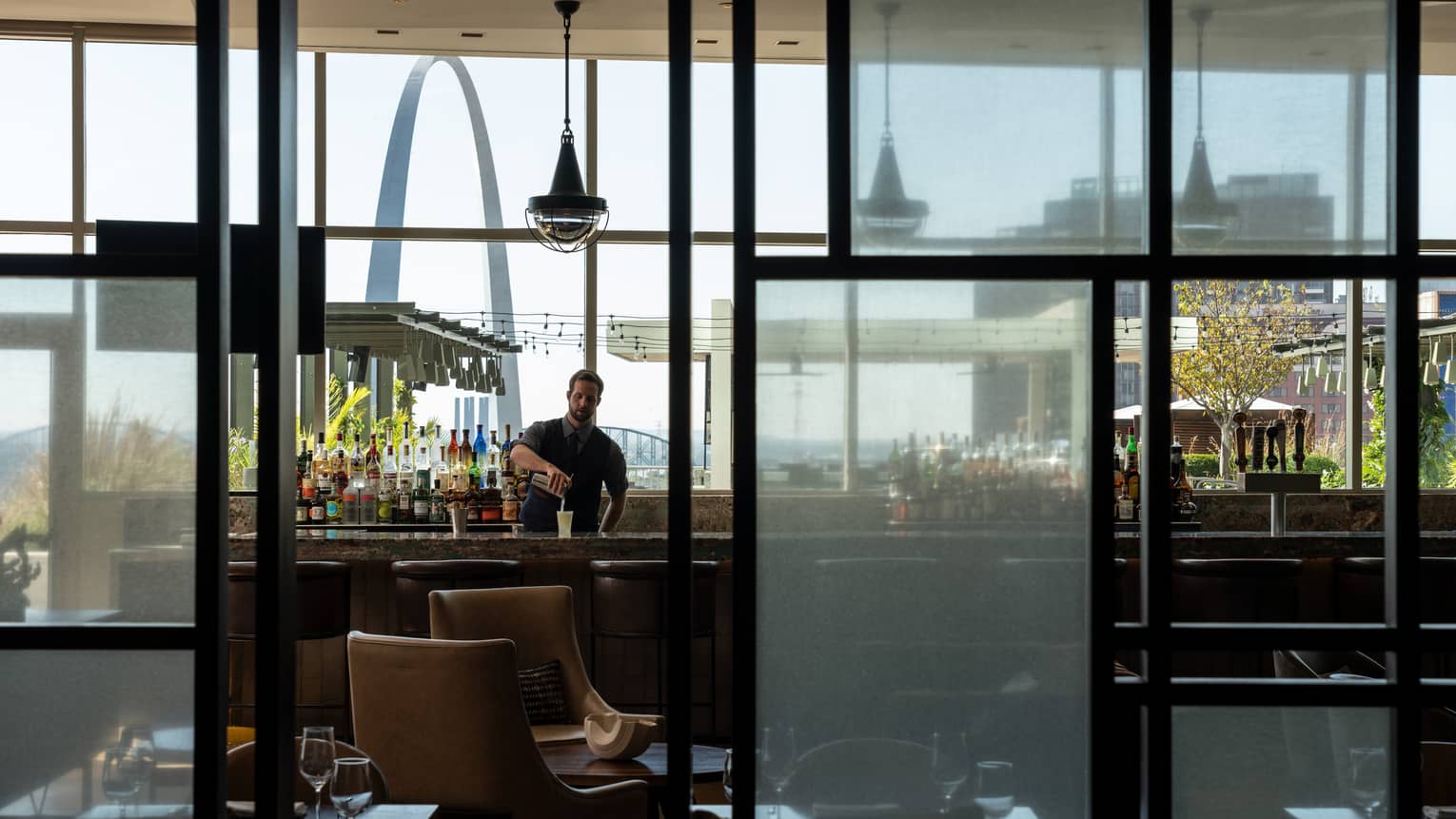 Looking through glass windows at cinderhouse reveals a bartender shaking up a drink at the bar 