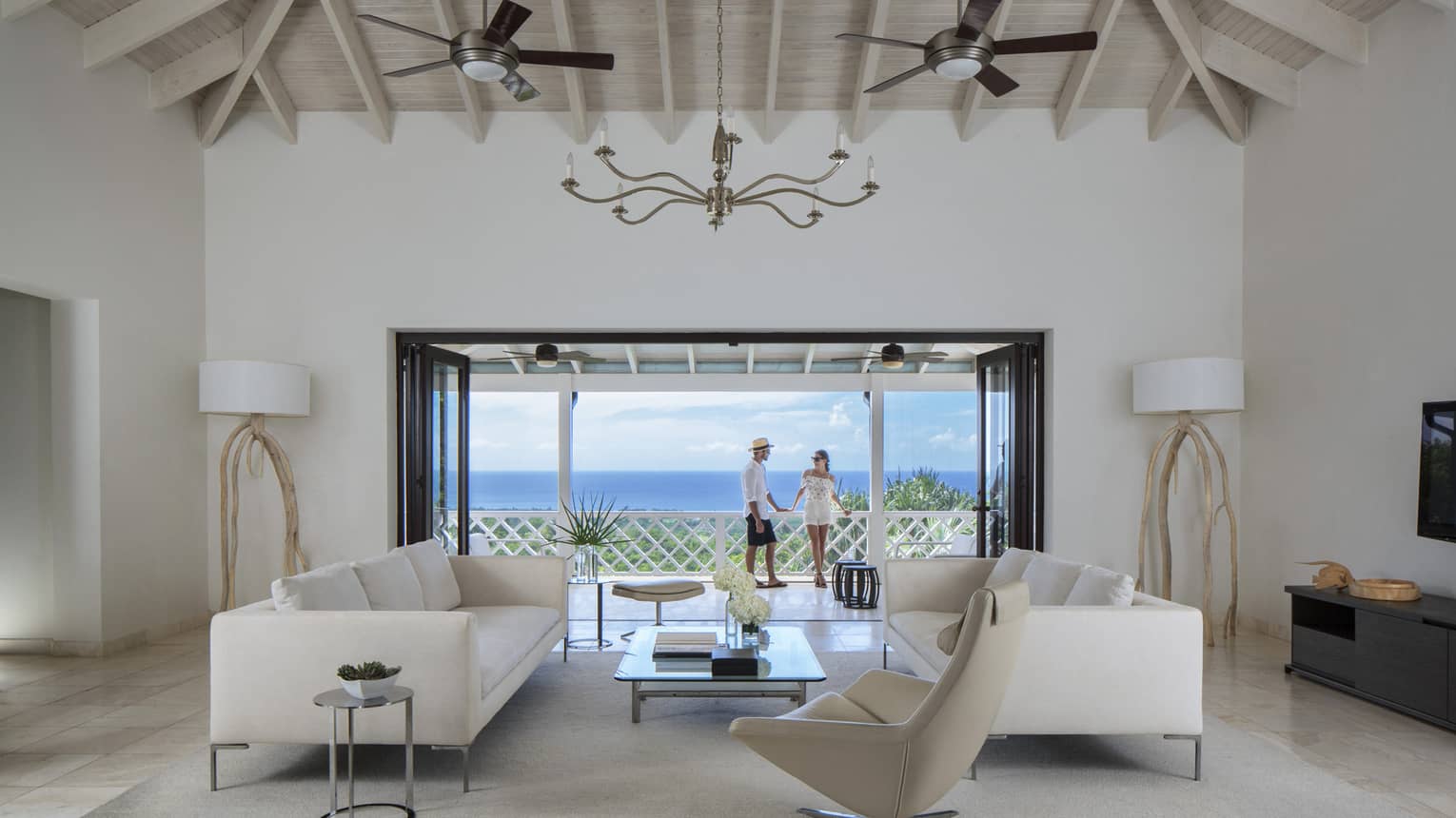 Living room with modern white furniture in front of open doors to sunny patio, couple
