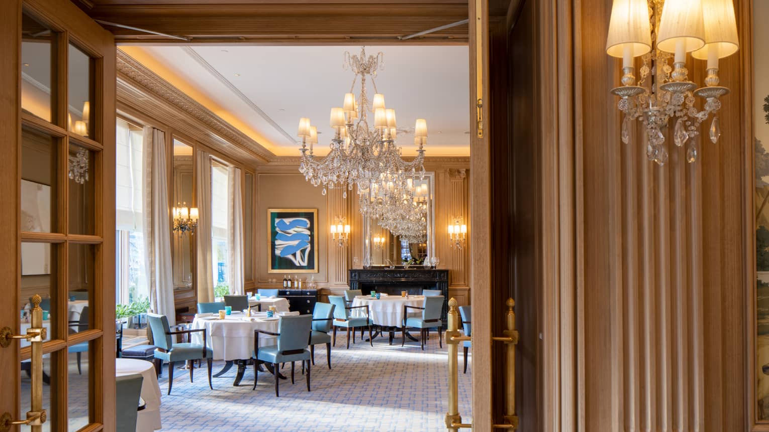 Dining area with blue chairs and round tables, crystal chandeliers and contemporary art