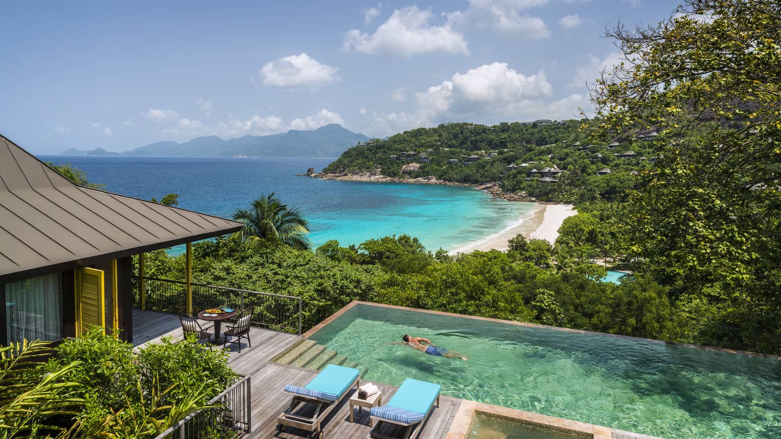 Two-bedroom Ocean View Suite deck, man swims laps in plunge pool, ocean and beach seen below
