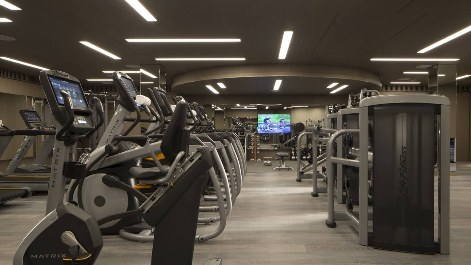 A fully-equipped gym with cardio and weight machines under dim lights.