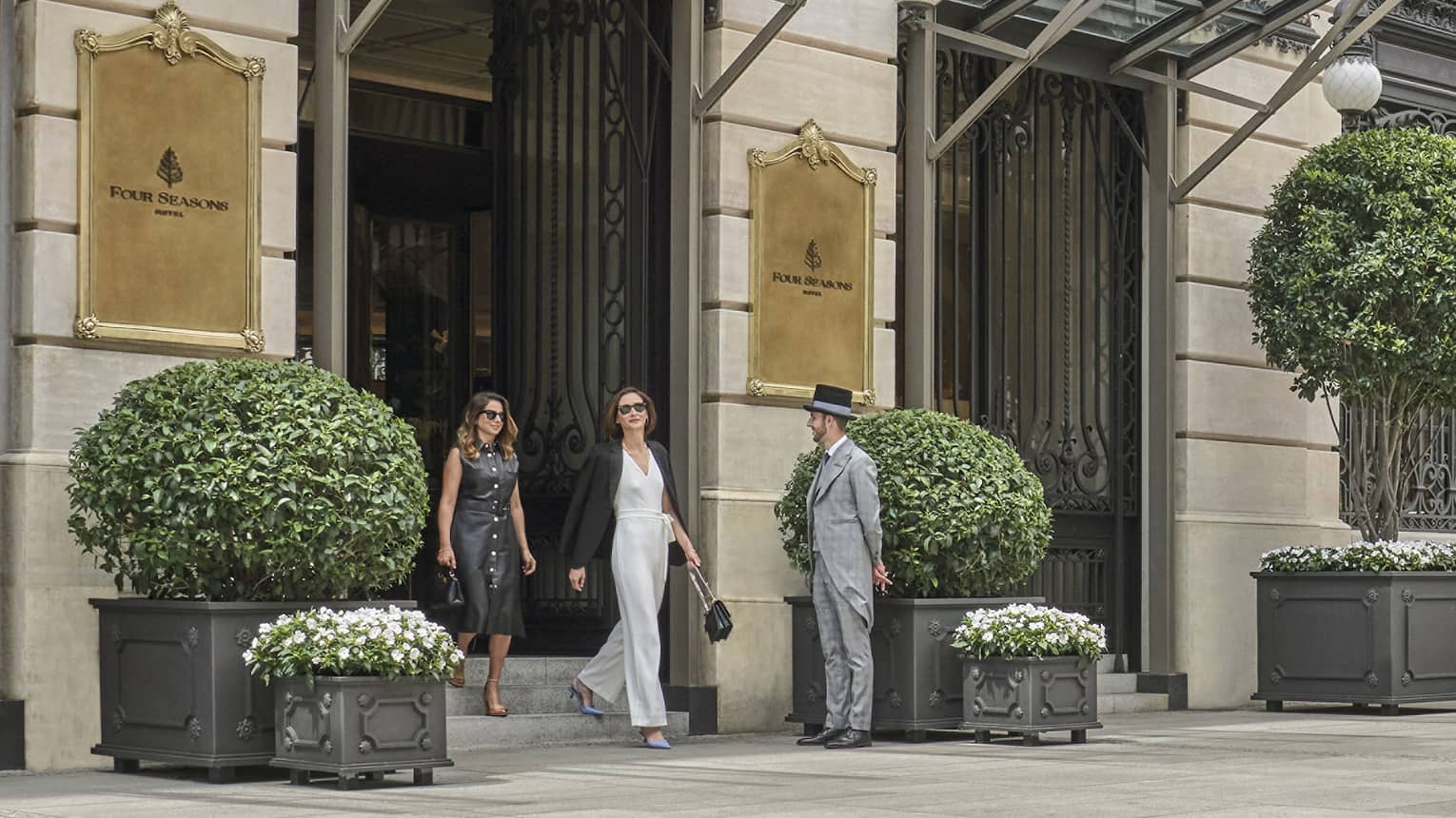 Four Seasons luxury hotel entrance with two guests walking out, doorman, glass canopies and large potted plants