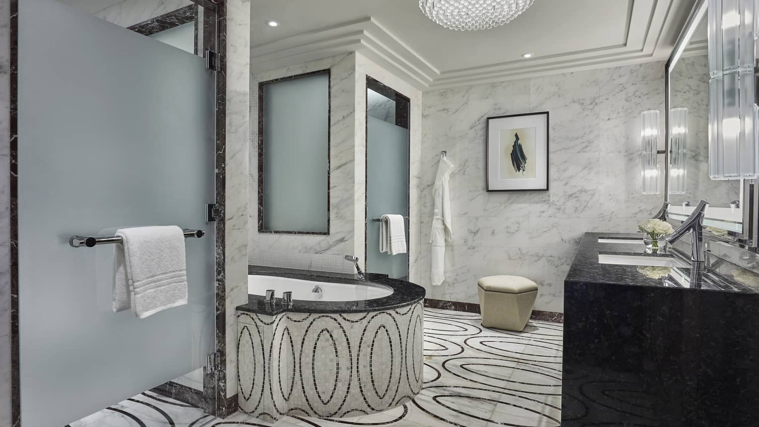 Elegant marble bathroom with a soaking tub, black granite vanity, frosted glass shower doors and intricate patterned flooring, accented by soft lighting