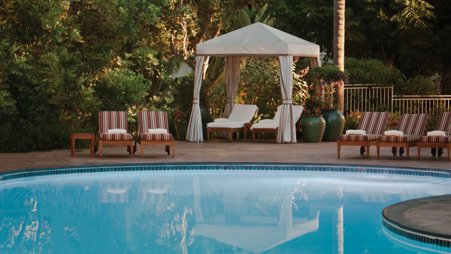 Striped pool chairs, white lounge chairs under white cabana curtains on swimming pool deck