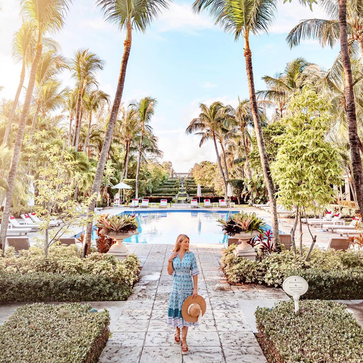 Person walking by a pool surrounded by palm trees at a Four Seasons tropical resort under a bright, sunny sky