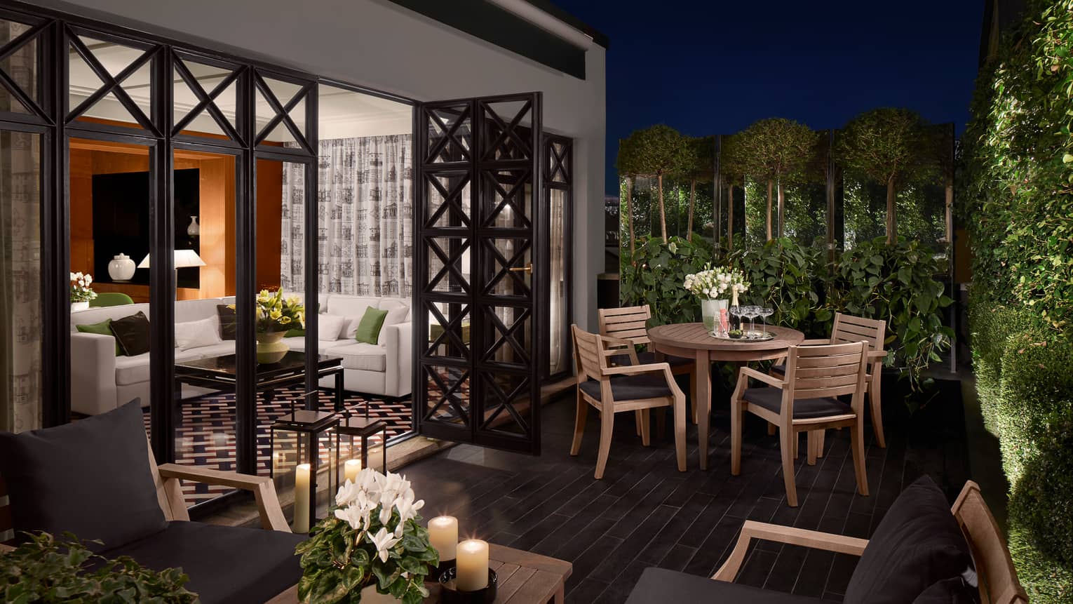 Balcony with wood tables and candles, chairs with black cushions, open doors to suite, white sofa