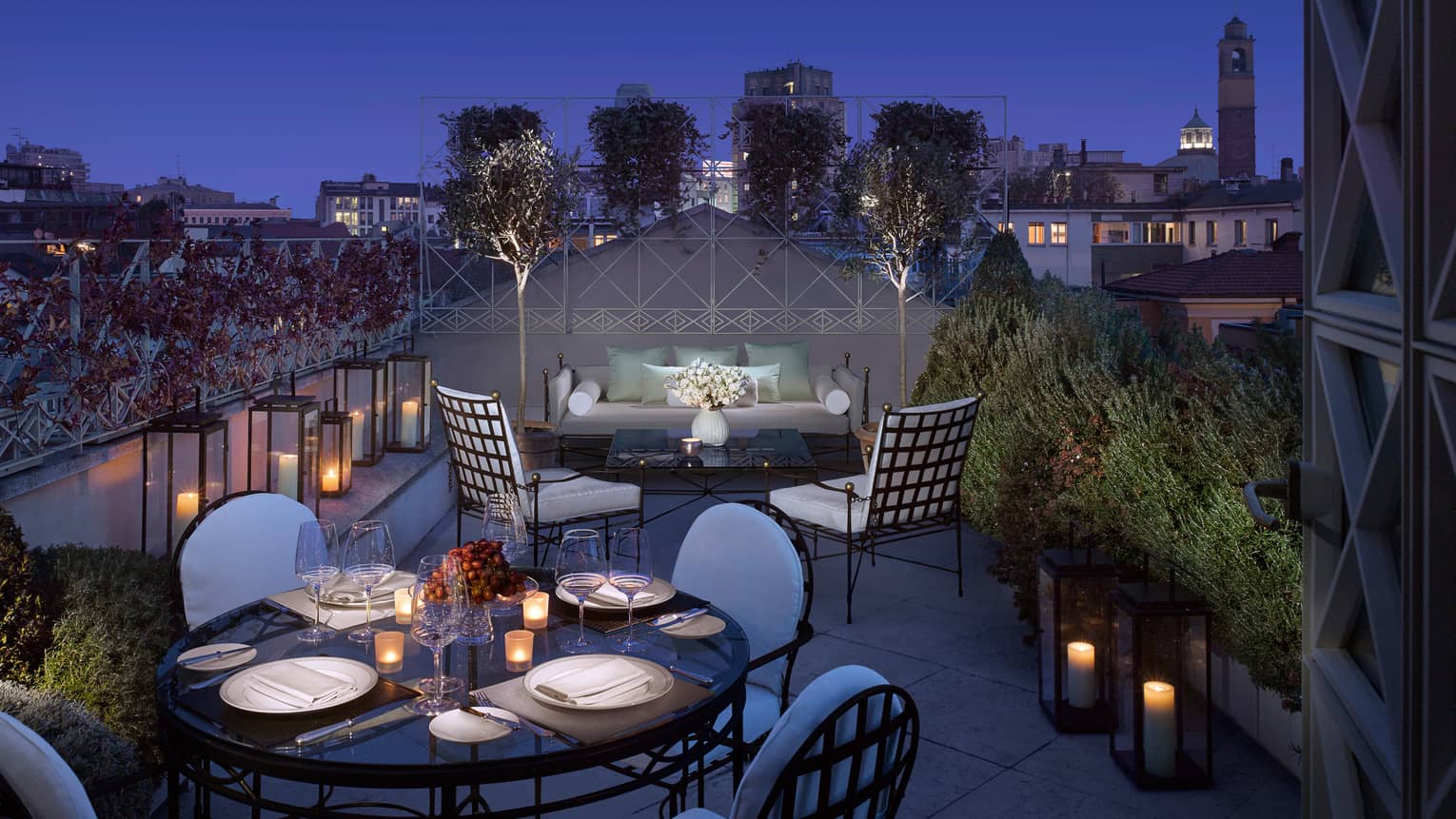 Penthouse Suite lantern-lined rooftop balcony, candle-lit dining table, patio sofa and chairs at night