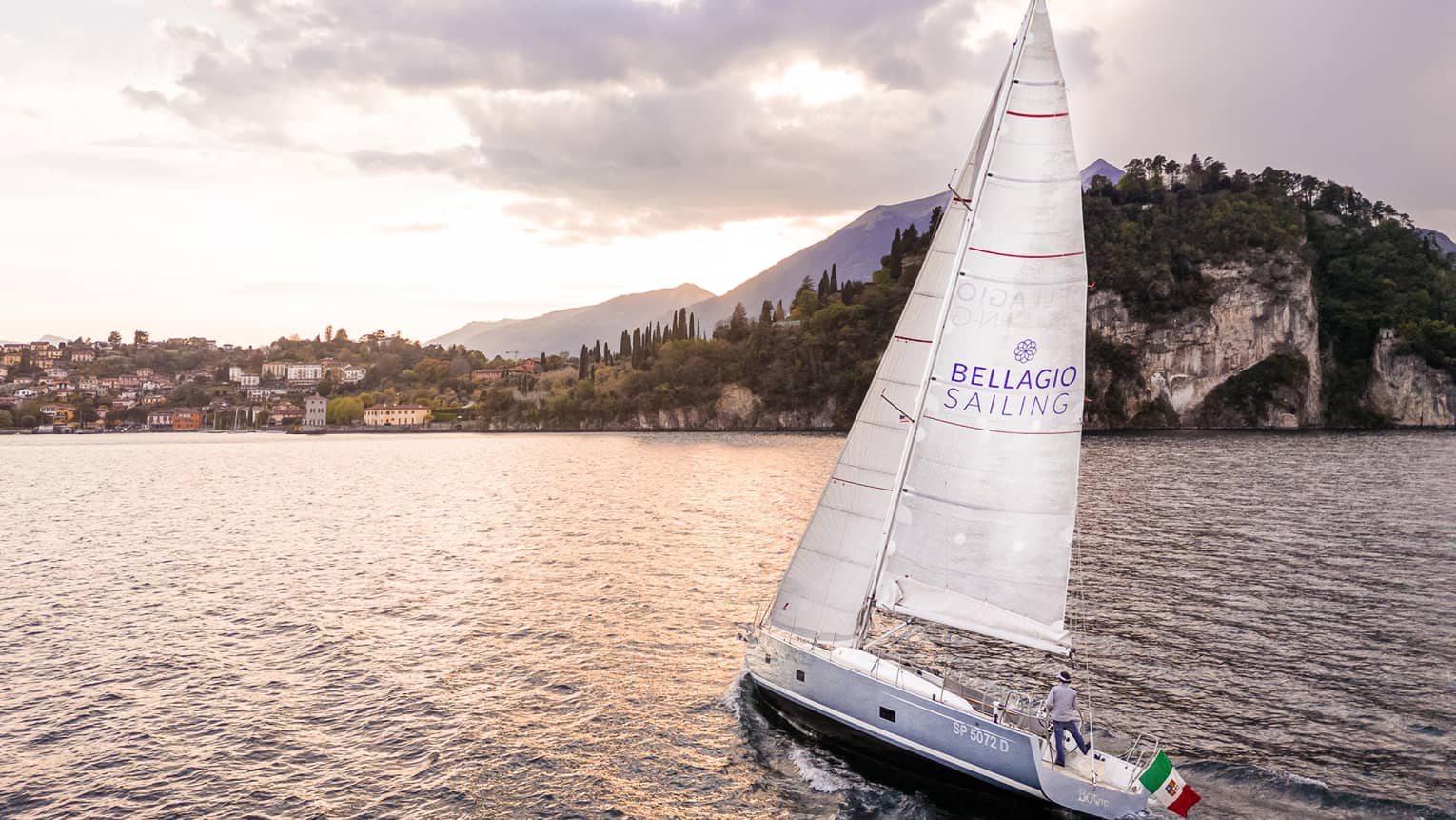 A sailboat on water near region with trees and buildings.