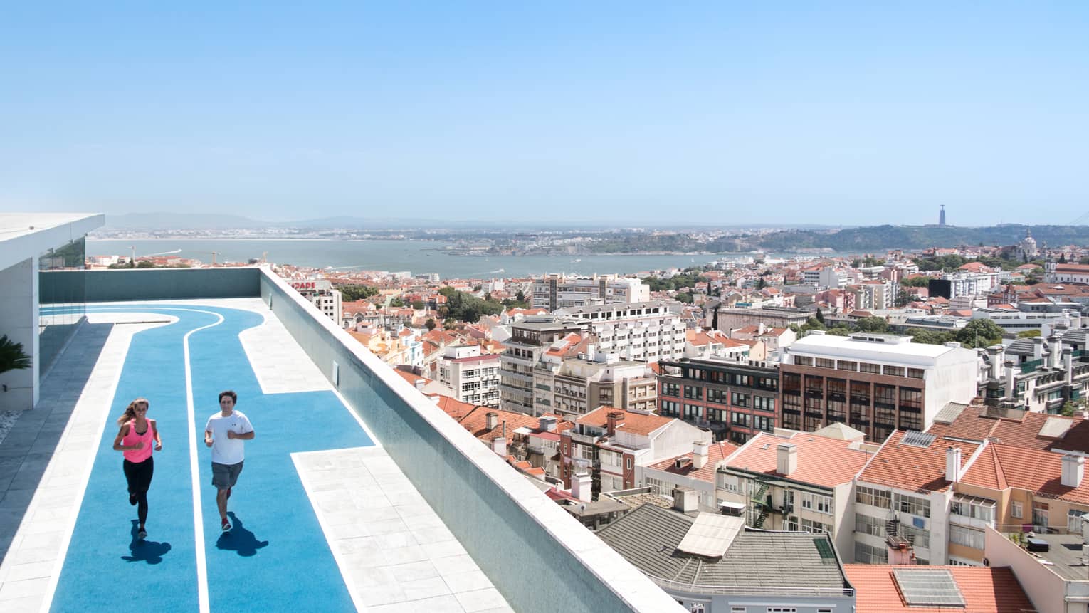 Two people run on blue, rooftop running track, overlooking Lisbon