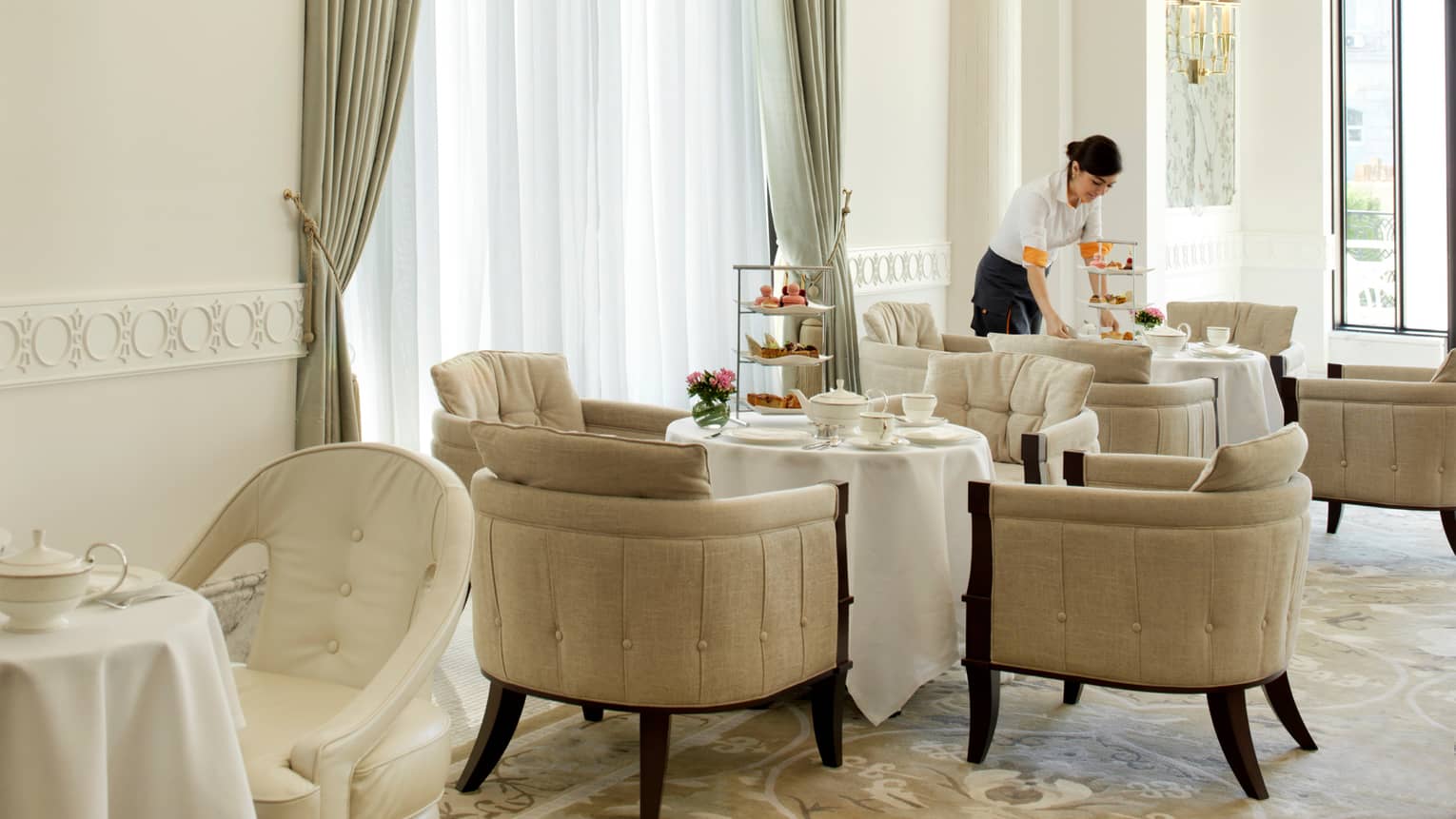Server sets three-tiered trays with desserts and tea pots on round table in sunny Piazza dining room