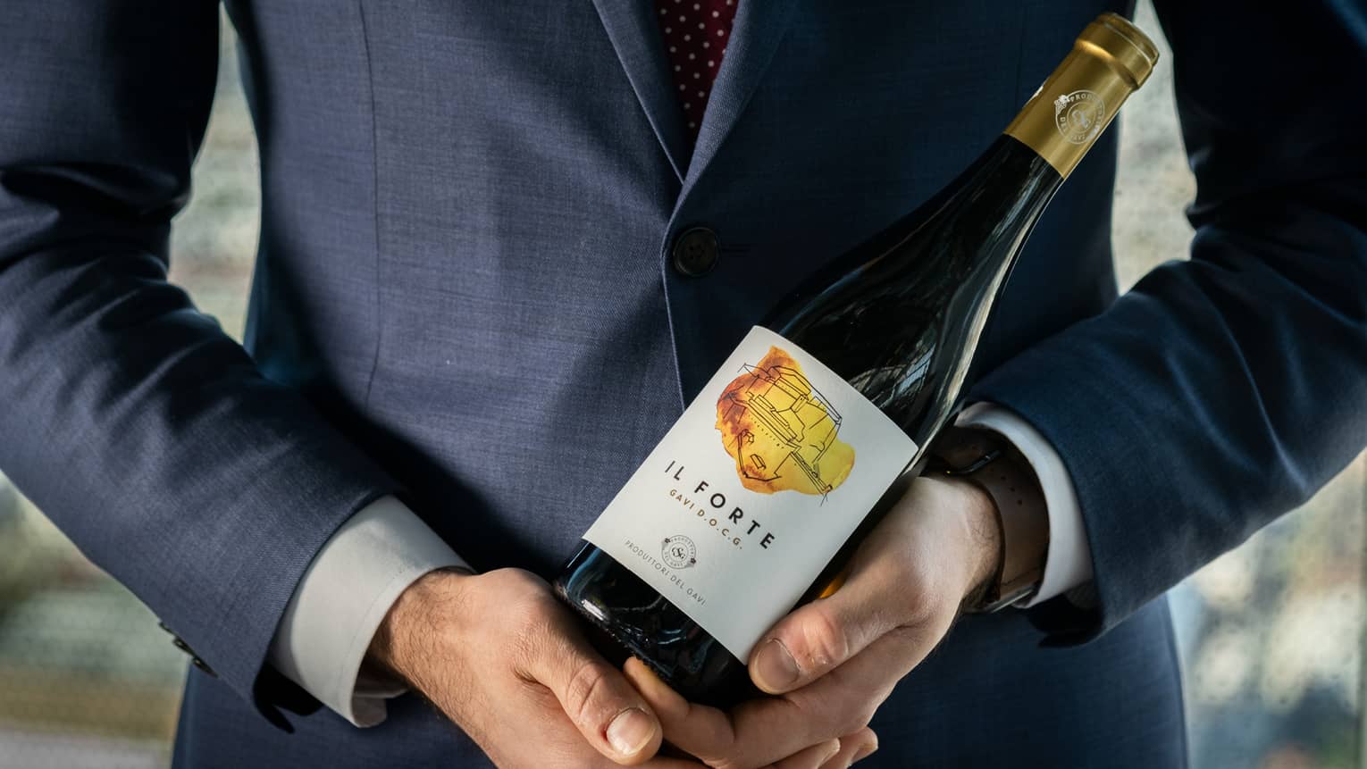 A man in a dark blue suit holding a bottle of wine.