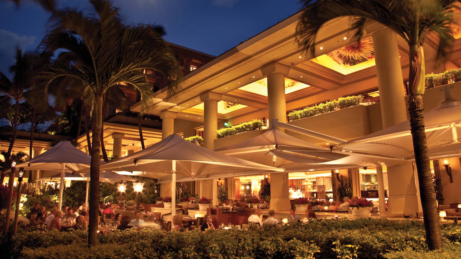 Exterior of hotel and restaurant patio with umbrellas illuminated at night