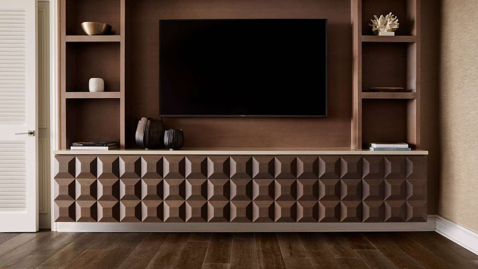 Wall-mounted TV with geometric wood cabinet and built-in shelves displaying decor items and books