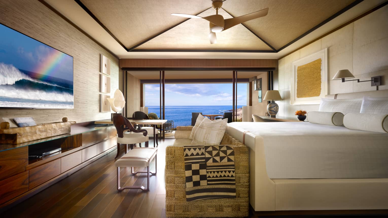 Oceanfront Room bed, small sofa and bench at foot, TV screen displaying ocean waves, rainbow