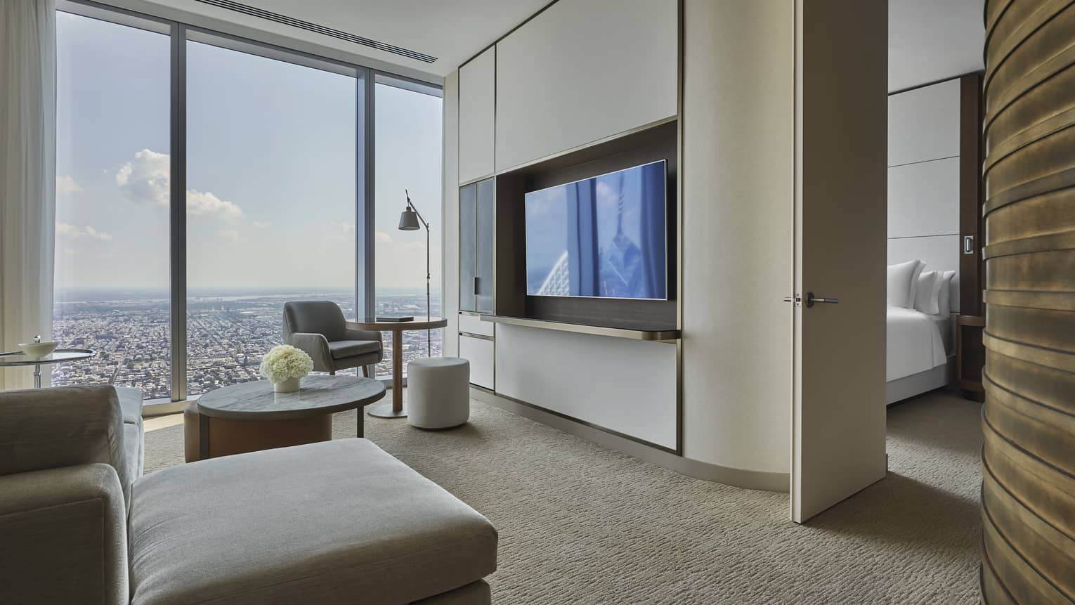 A living room space with a grey sofa, large windows and a large televisoin.