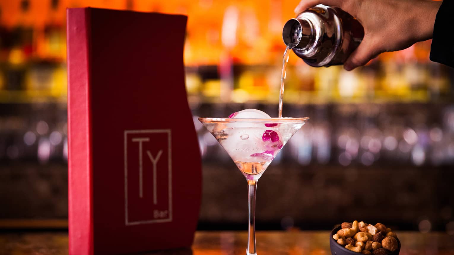 Red Ty Lounge menu on bar, bartender pours liquor into tall martini glass