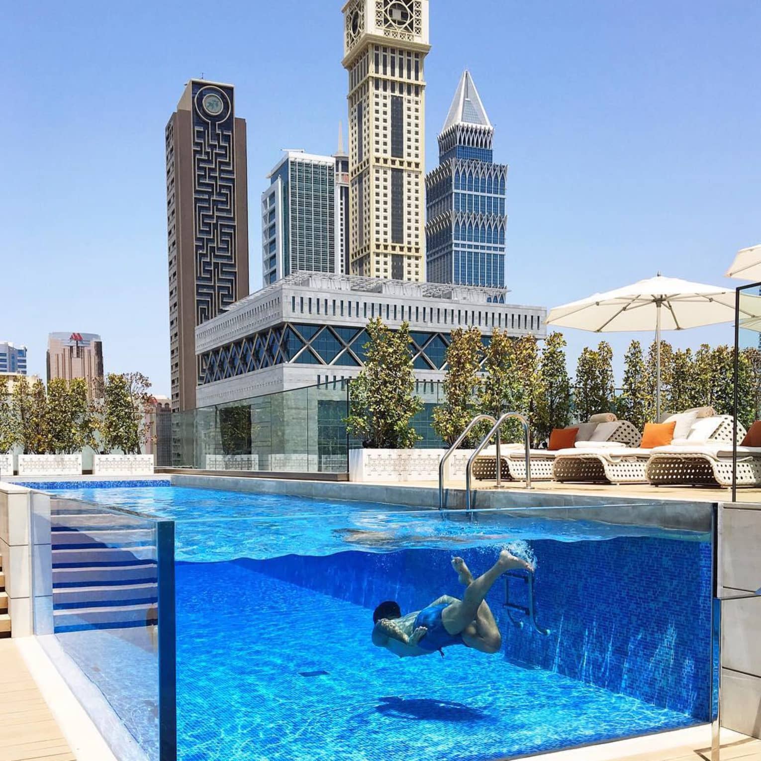 Man swims underwater in raised glass plunge pool on hotel deck