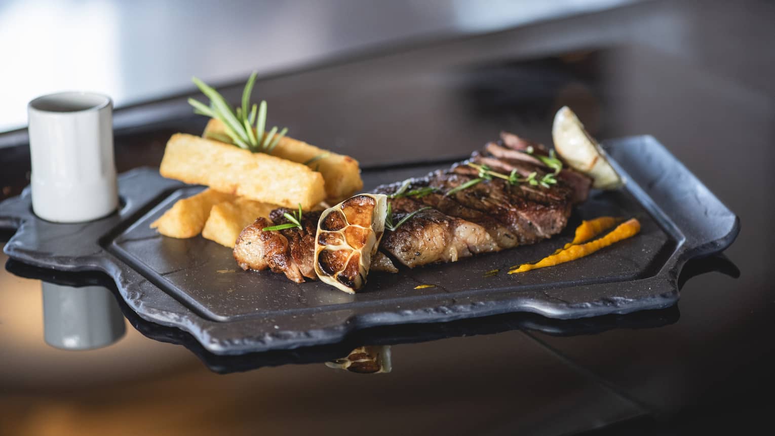 Grilled meat, lemon wedges with frites on slate platter